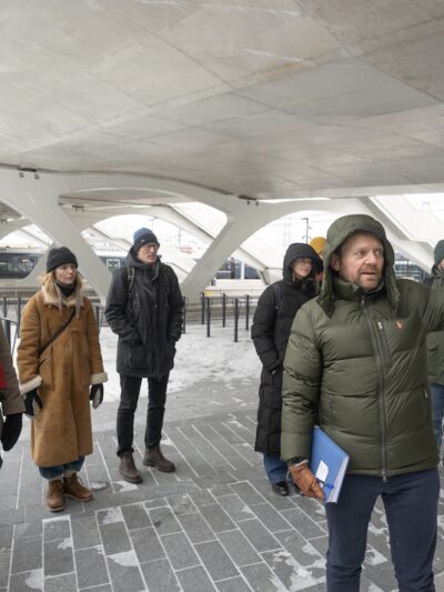 Mann peker og står foran en gruppe mennesker som er på omvisning. Foto.